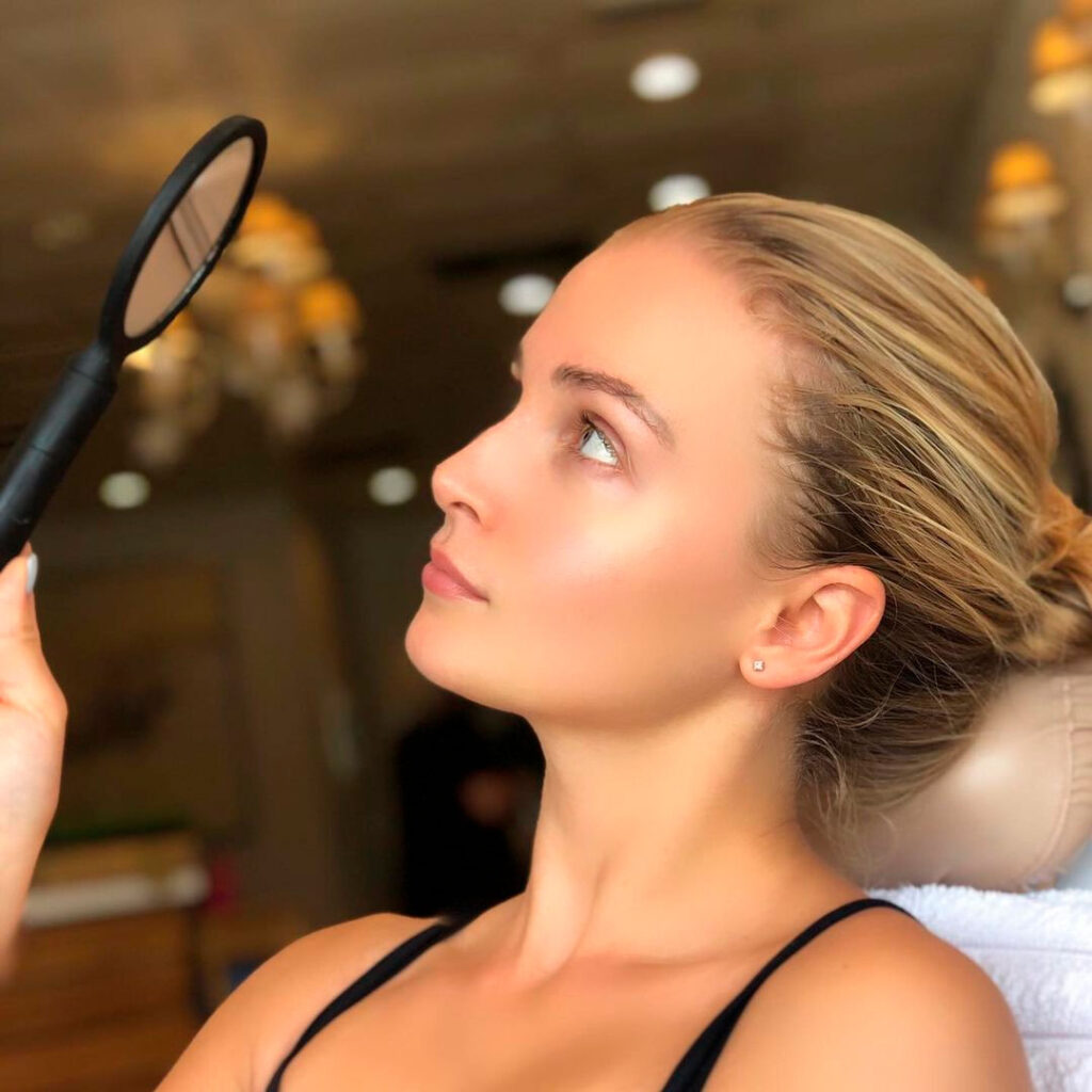 A woman looking into the mirror while holding onto a hair brush.